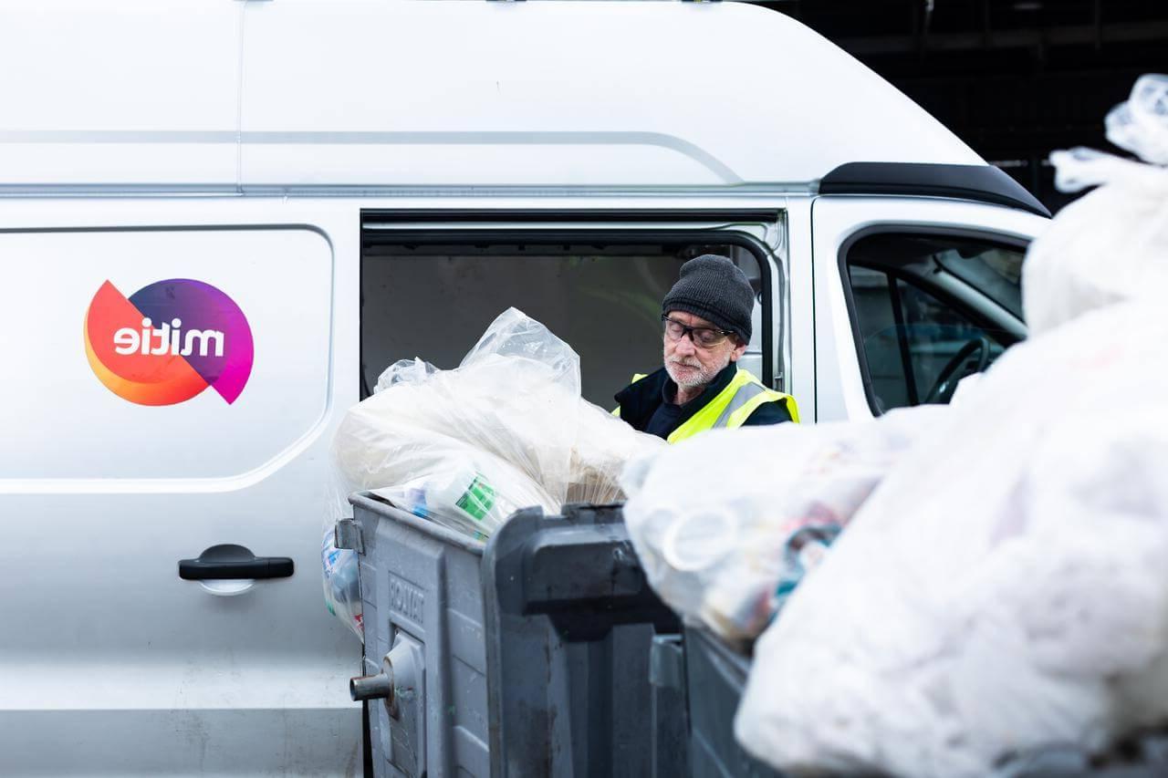 Mitie employee removing waste in plastic bags from roller bins, 旁边是一辆有米蒂标志的货车